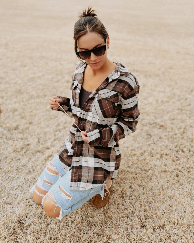 41 year old woman wearing ripped jeans and a flannel kneeling in the grass staring at the ground